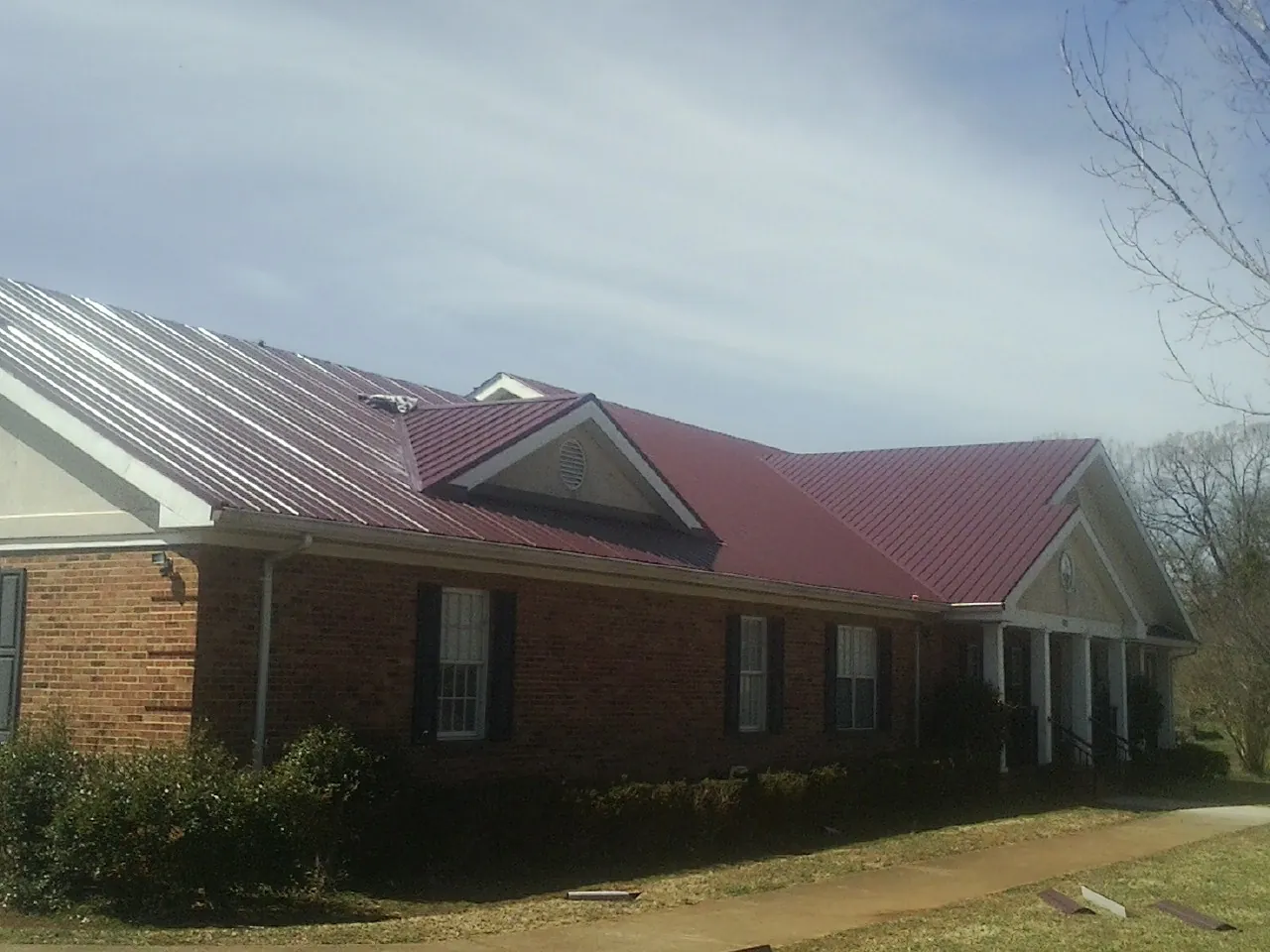 Red metal roof with gabled entries on a long brick building, from a Hail Damage Roof Repair job in Stockton