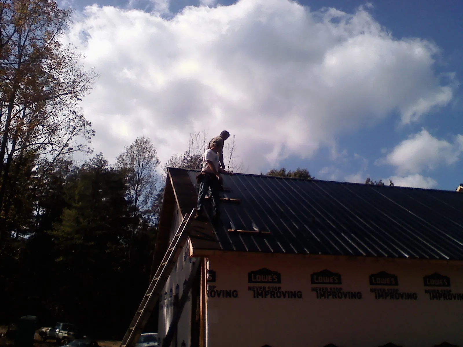 Roofer fastening dark metal panels high against a cloudy sky, from a Roof Inspection job in Stockton